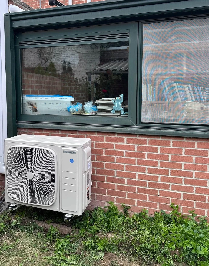 Unité extérieure de pompe à chaleur air/air Thermor posée sur plots antivibratiles contre une façade en brique