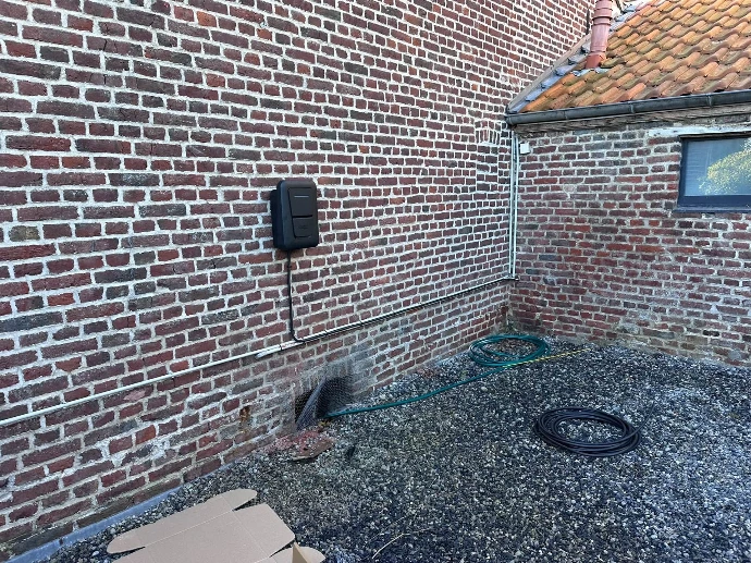 Borne de recharge Hager 7 kW installée sur un mur en brique dans une cour à Rumegies