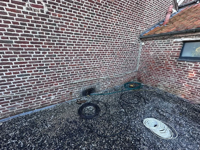 Ligne électrique dédiée tirée en extérieur le long d'une façade en brique jusqu'à l'emplacement de la borne